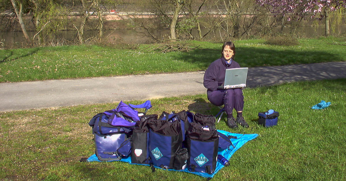 Beate Steger sitzt auf dem Campingplatz am Neckar mit Laptop und vielen Radtaschen von Ortlieb